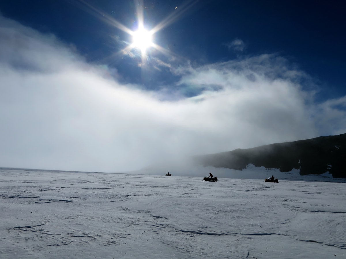 a landscape shot of the scientists on snowmobiles.