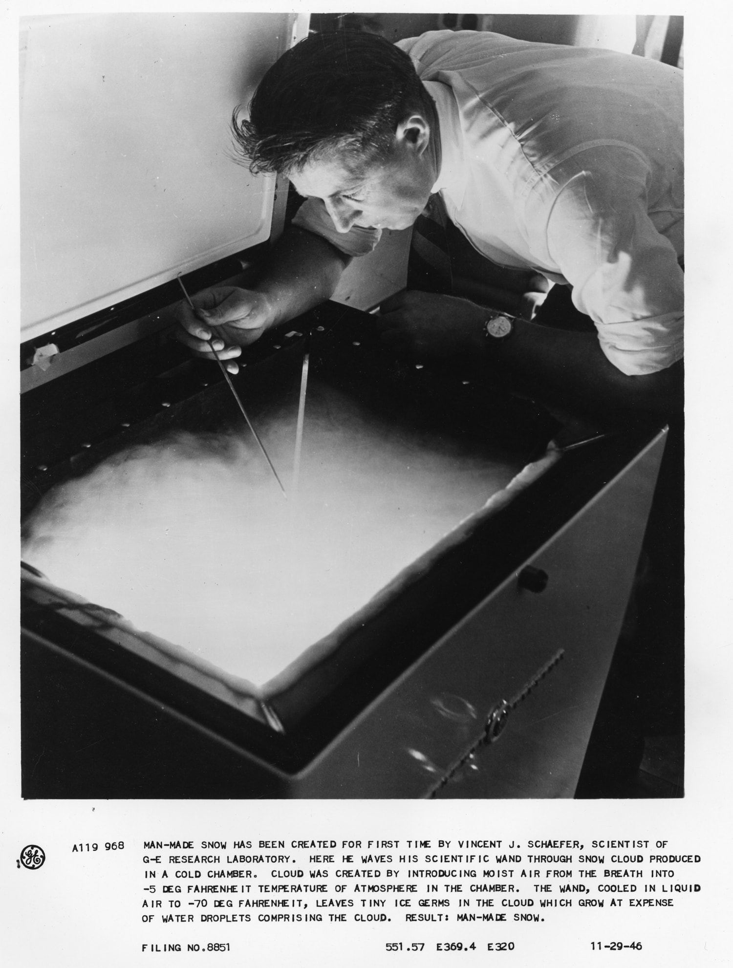 Vincent Schaefer peers into a glowing box with mist on the inside, inserting a rod into the container.